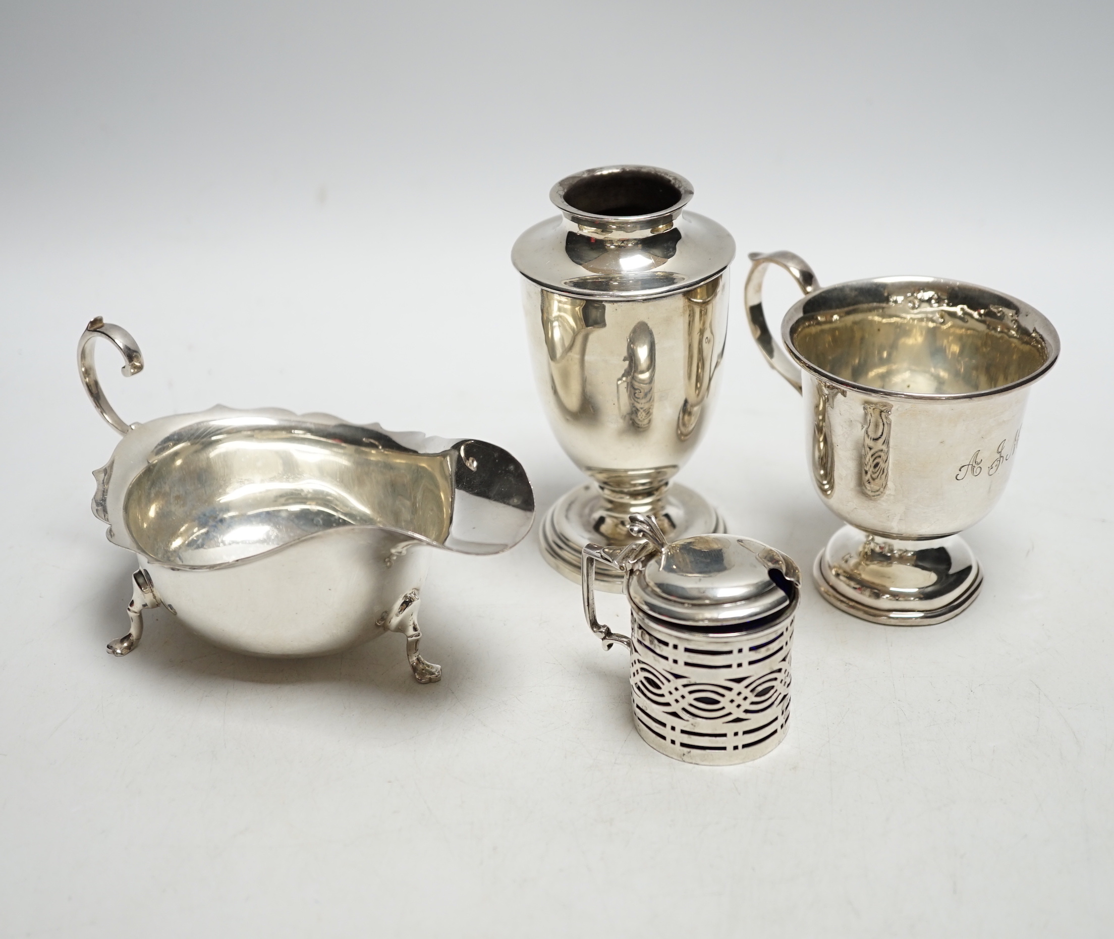 Four pieces of George V silver:- a sauceboat, a mustard pot, a vase and a cup.